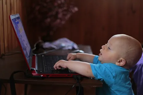 Toddler typing on a laptop with a focused expression.