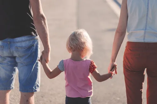 A small child holds hands with two adults while walking.