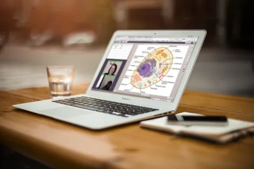 Laptop on wooden table with a diagram on the screen, next to a notebook and glass of water.